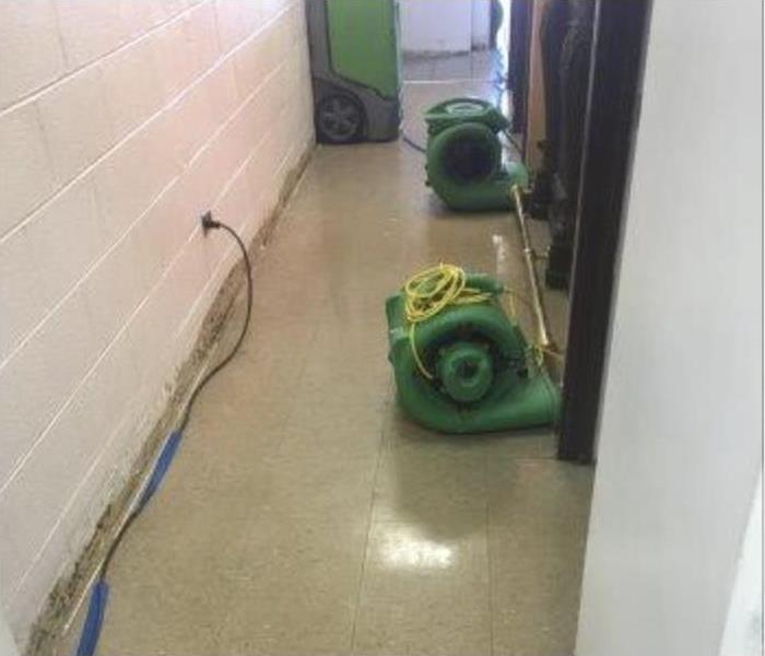 Two air movers and a dehumidifier placed in the hallway of a building.